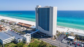 Un grand hôtel avec de nombreuses étages, offrant une vue sur la plage, doté de parkings et avec une jetée en arrière-plan.