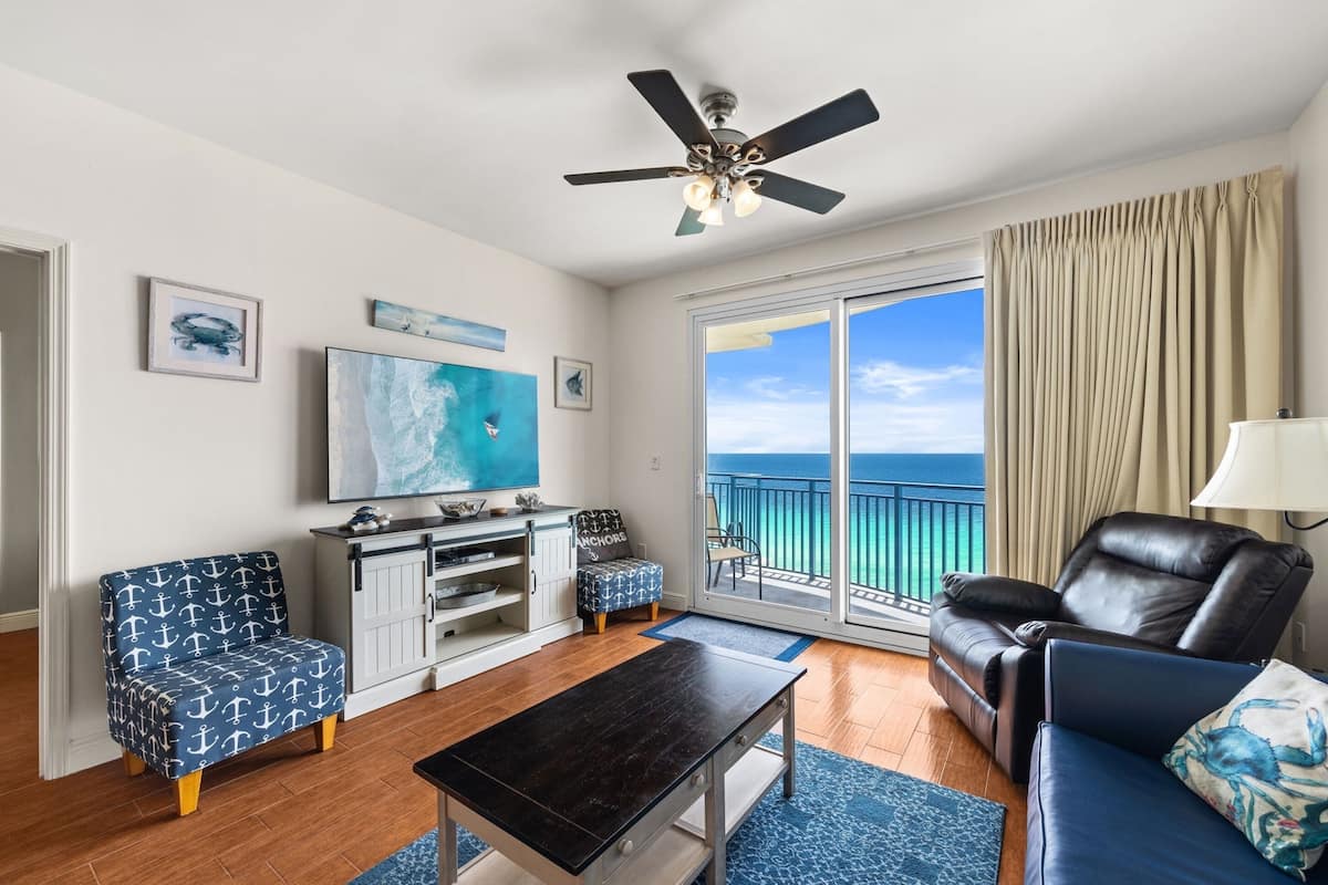 Ein Wohnzimmer mit Meerblick, Deckenventilator, einer Couch, einem Couchtisch und einem Fernseher.
