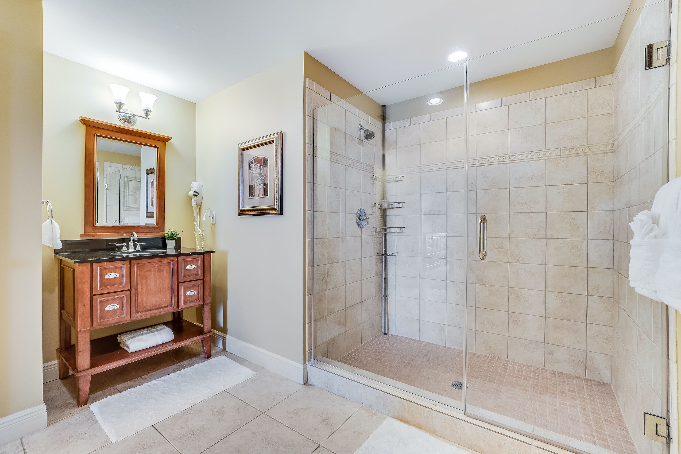 Un baño con tocador de madera, cabina de ducha con mampara de vidrio y un cuadro en la pared.