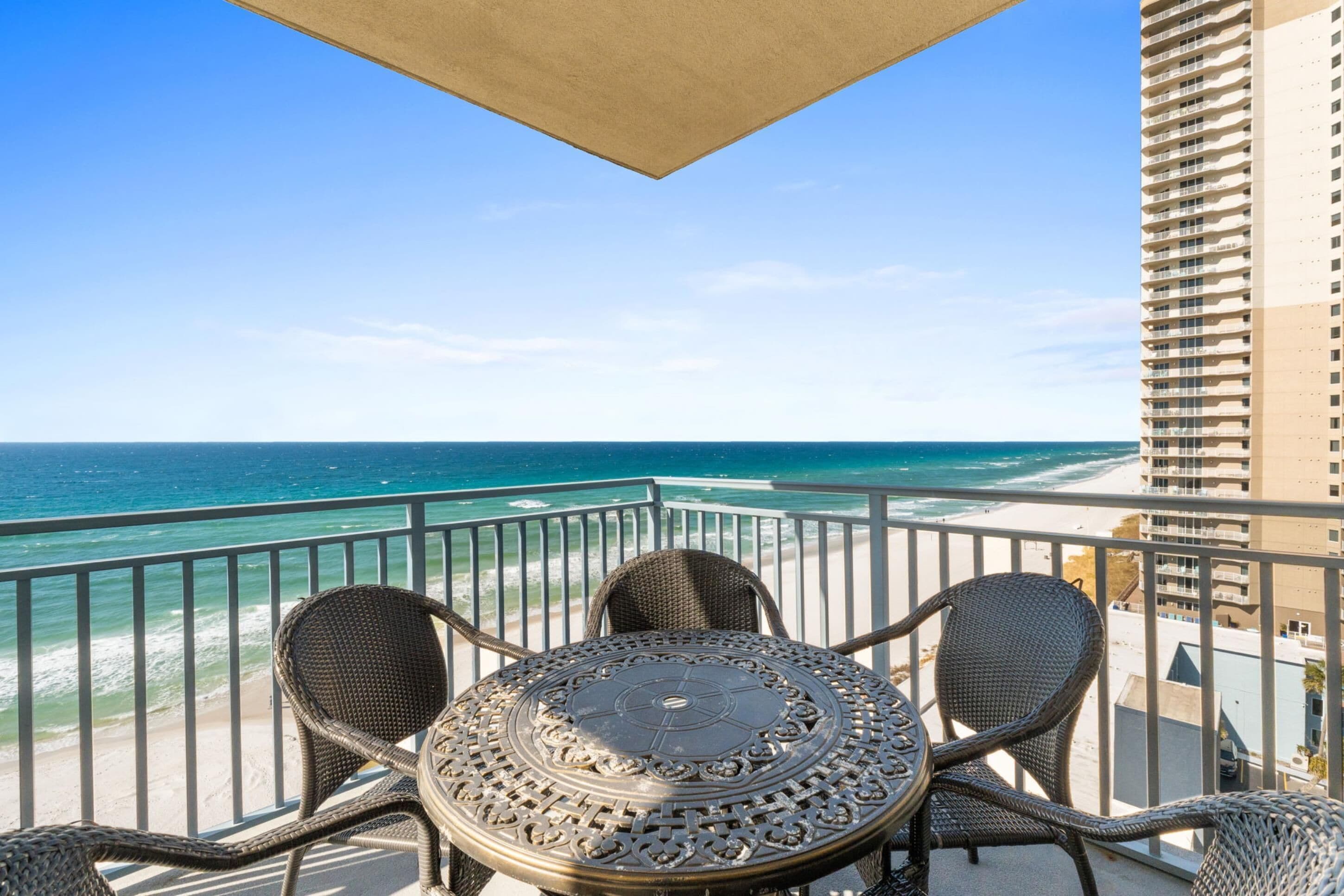 A balcony with a round table and wicker chairs overlooking a beach and ocean.