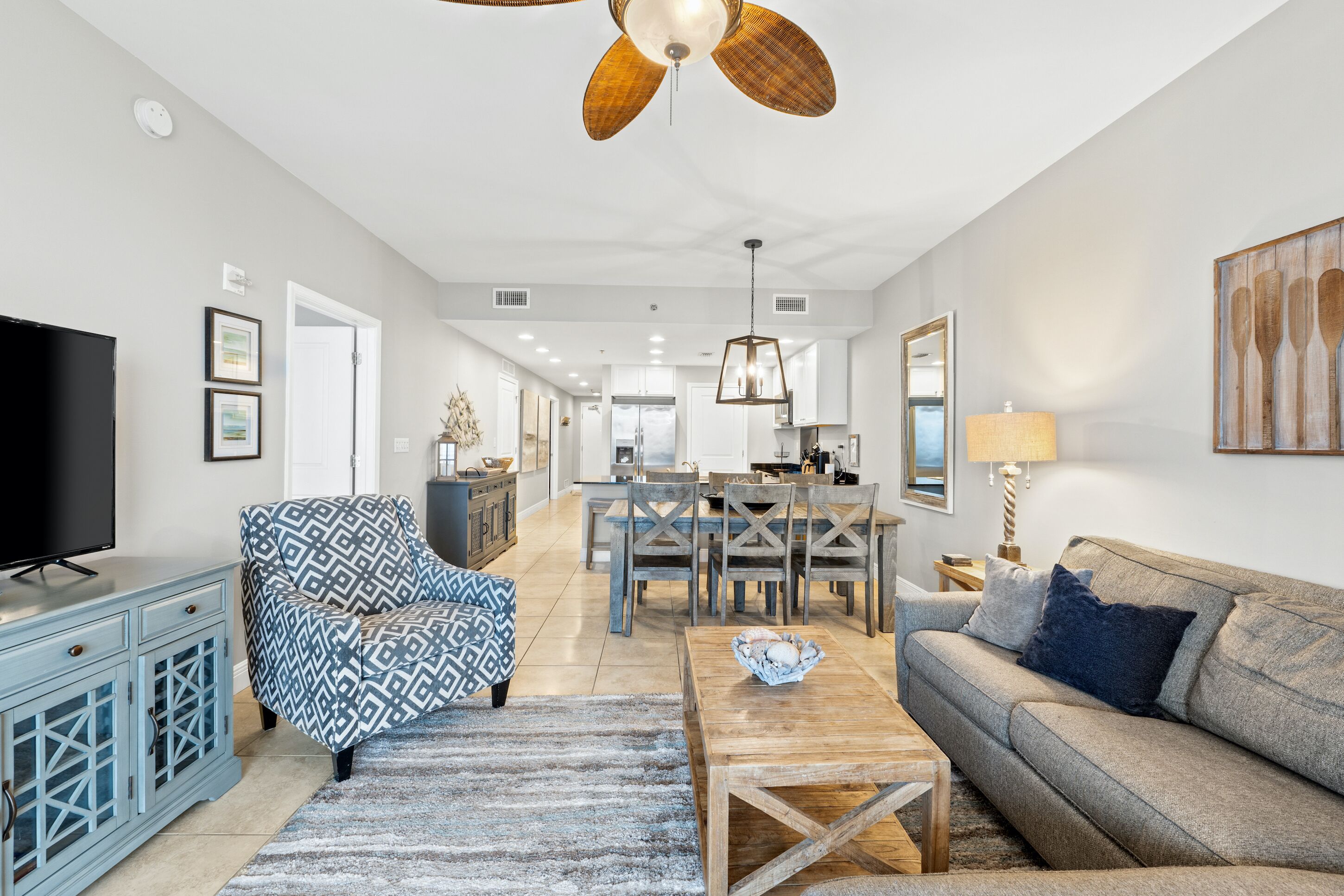 A spacious living room with a television, patterned armchair, wooden coffee table, and a sofa.