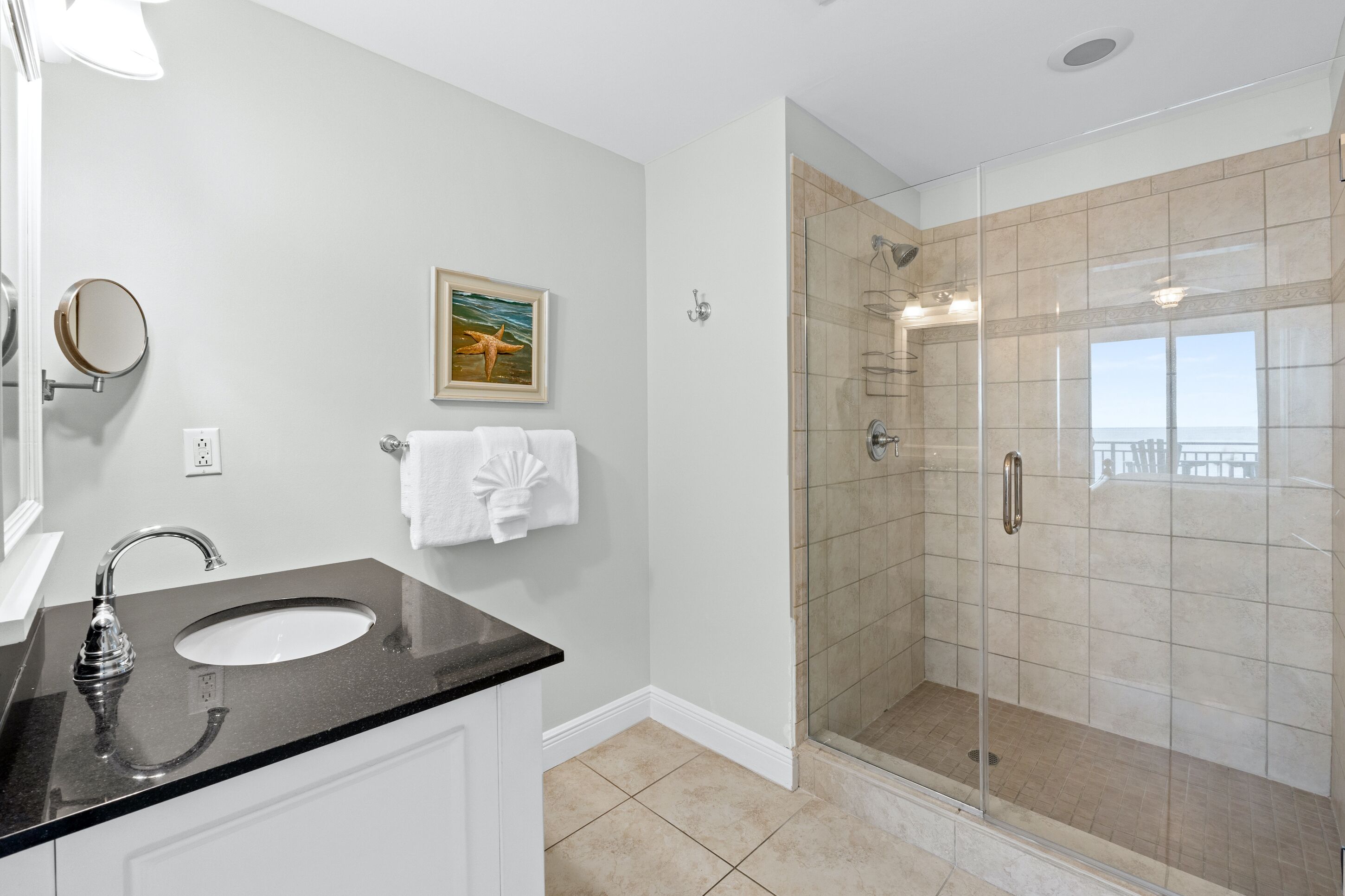 A bathroom with a glass-enclosed shower, a sink with a black countertop, and a framed picture on the wall.