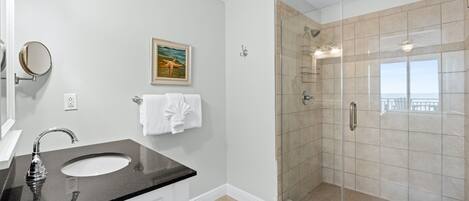 Ein Badezimmer mit einer Duschkabine, einem Waschbecken mit schwarzer Arbeitsplatte und einem gerahmten Bild an der Wand.
