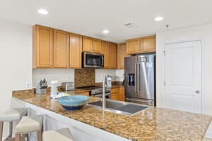 A kitchen with granite countertops, wooden cabinets, stainless steel appliances, and a white door.