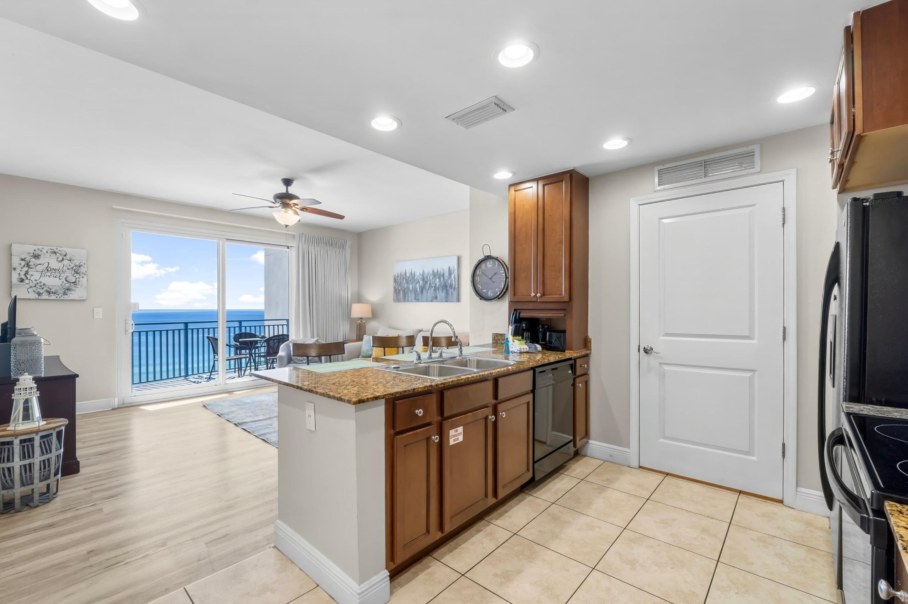 A modern kitchen with a large island, built-in appliances, and a view to the balcony.