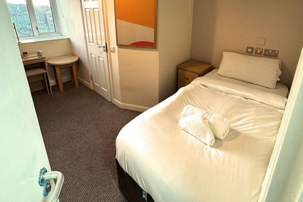 A hotel room with a bed, a desk, a chair, a window, and a door.