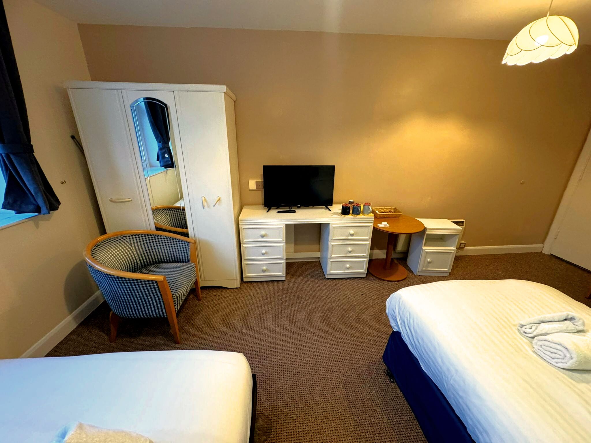 Une chambre d’hôtel avec deux lits, un bureau avec une télévision, une chaise, une armoire et une petite table avec une lampe.