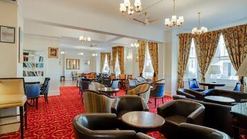 A hotel lobby with a red carpet, multiple seating areas, chandeliers, and large windows with curtains.