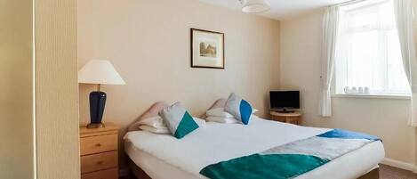 A hotel room with a bed, a bedside table with a lamp, a television, and a window with curtains.