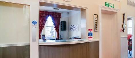 A reception area with a clock, a reception desk, a window with curtains, and an exit sign.