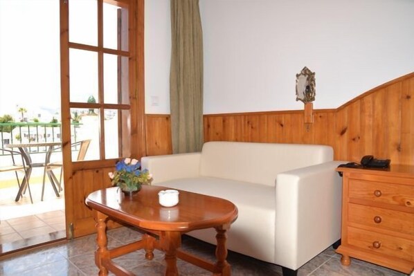 A room with a wooden paneled wall, a white sofa, a wooden table with a vase of flowers, and a wooden dresser. - Hotel José Cruz (Nerja)