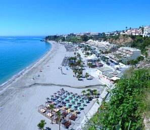 A coastal resort with a beach, multiple-story buildings, and a parking area with umbrellas. - Hotel José Cruz (Nerja)