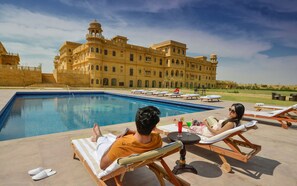 A poolside area with lounge chairs and a large building in the background.