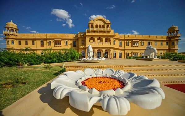 A large, ornate building with a central fountain and statues, surrounded by well-maintained gardens.