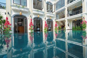 Um edifício com várias andares, piscina central, varandas e plantas ao ar livre.