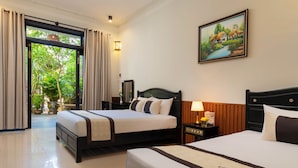 A hotel room with two beds, a large window with curtains, a painting on the wall, and a small table with a lamp and a sign. - Green Tea Homestay (Da Nang)