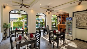 A restaurant with tables and chairs, ceiling fans, and a refrigerator. - Green Tea Homestay (Da Nang)