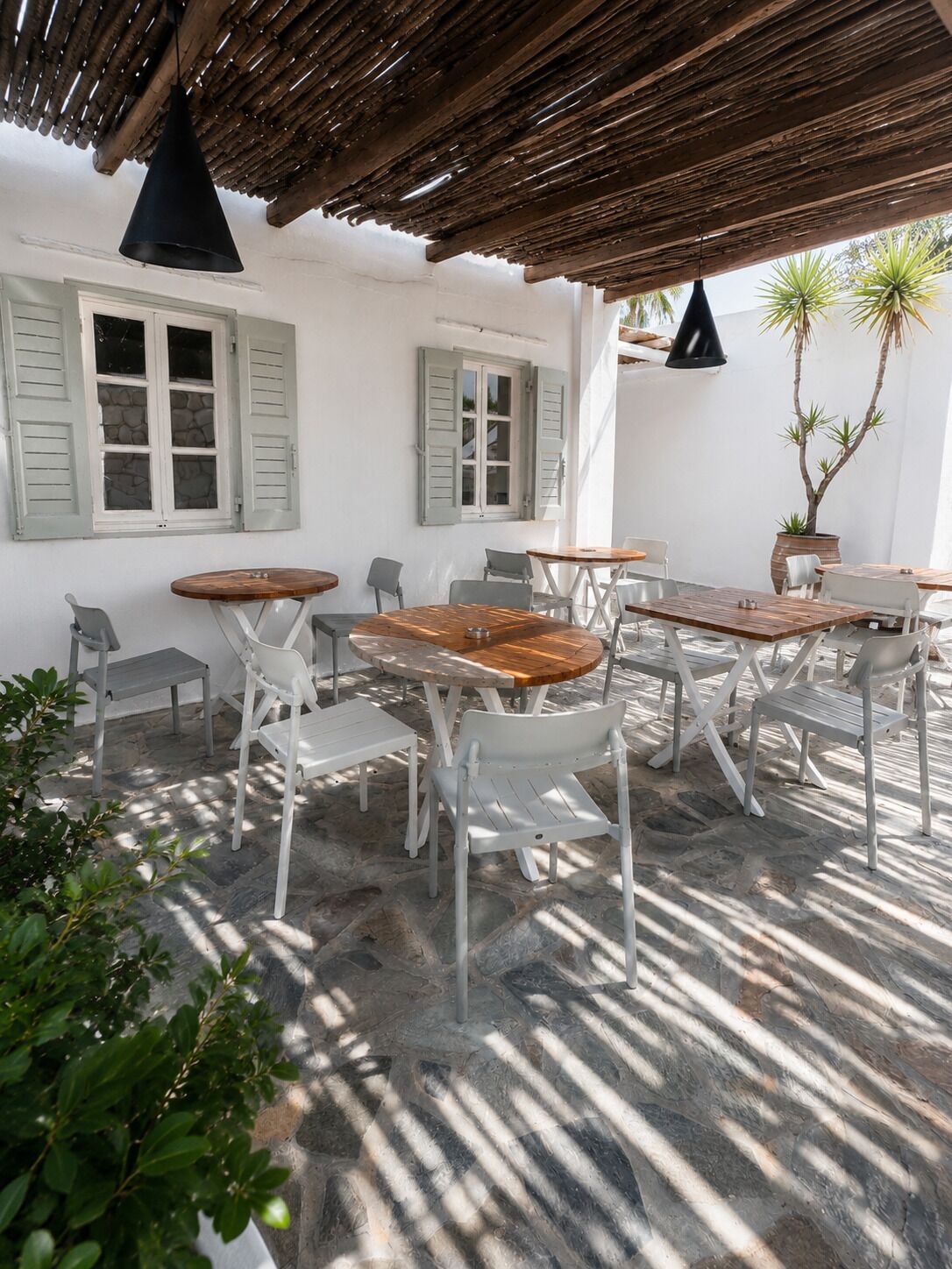 An outdoor patio with stone flooring, white furniture, and a wooden pergola.