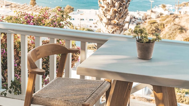 Een houten stoel en tafel op een balkon met uitzicht op de kust, met boten en gebouwen.