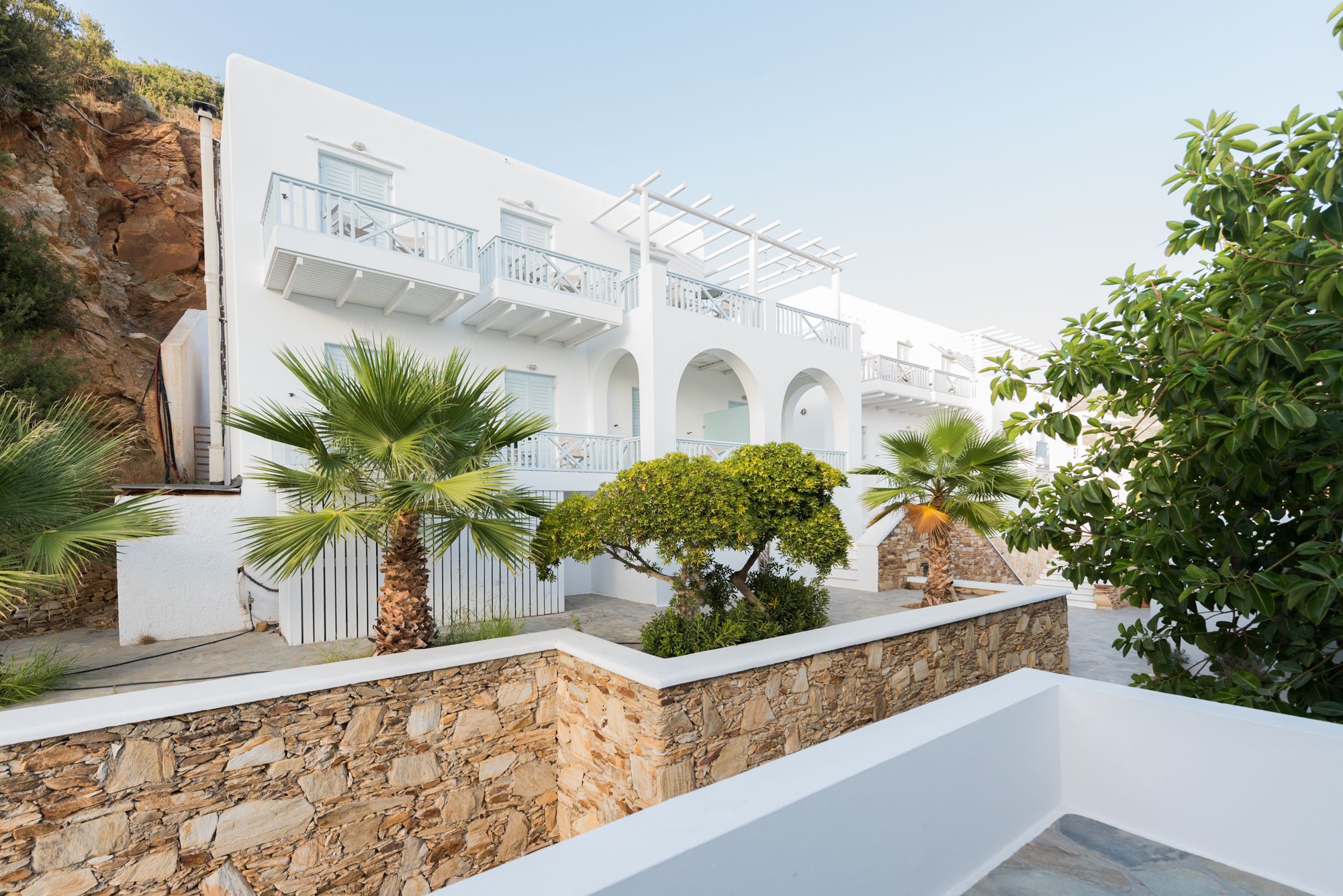 Un bâtiment blanc doté de balcons, de murs en pierre et de plantes tropicales.