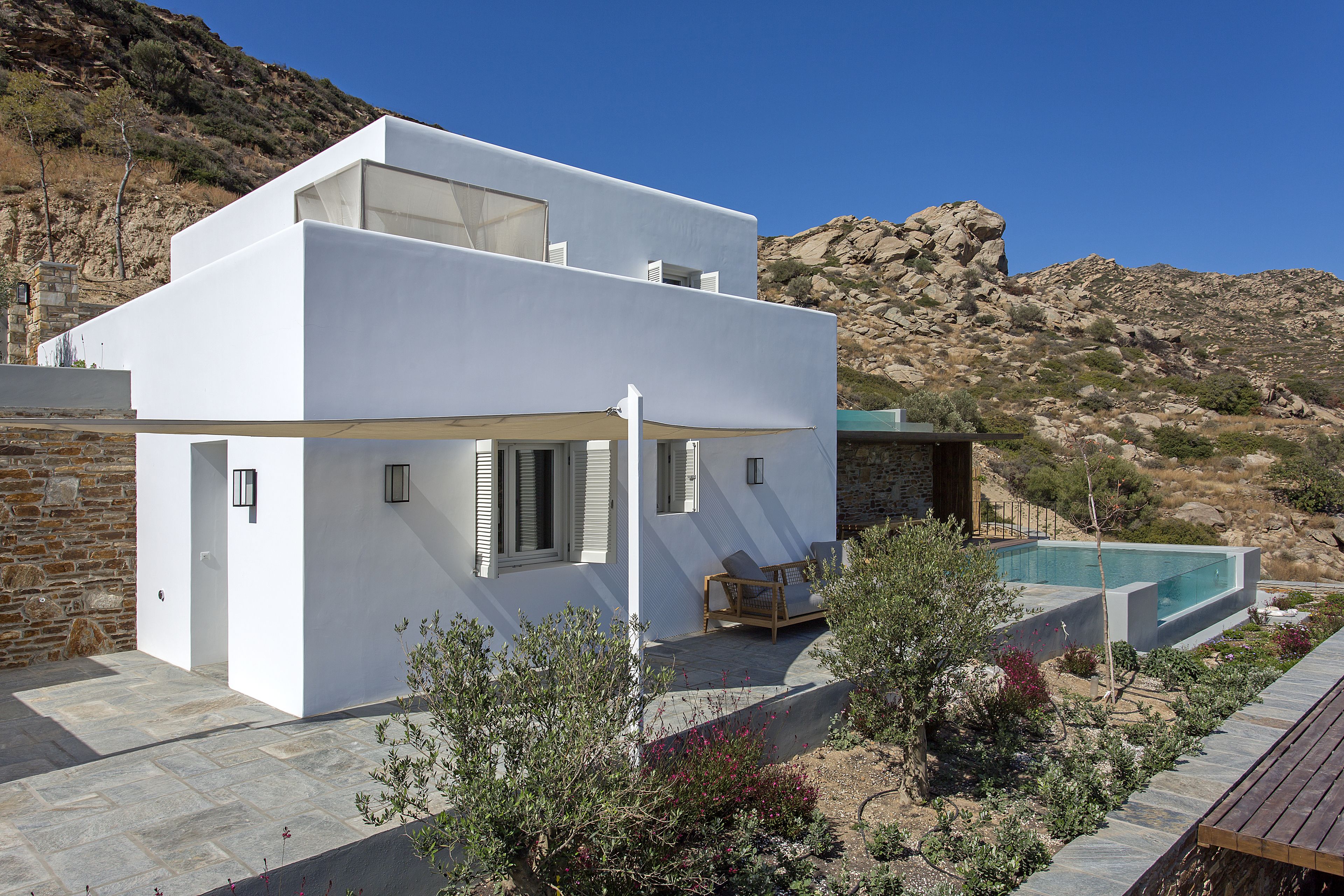 Un edificio moderno blanco con piscina, escalones de piedra y vistas a colinas rocosas.