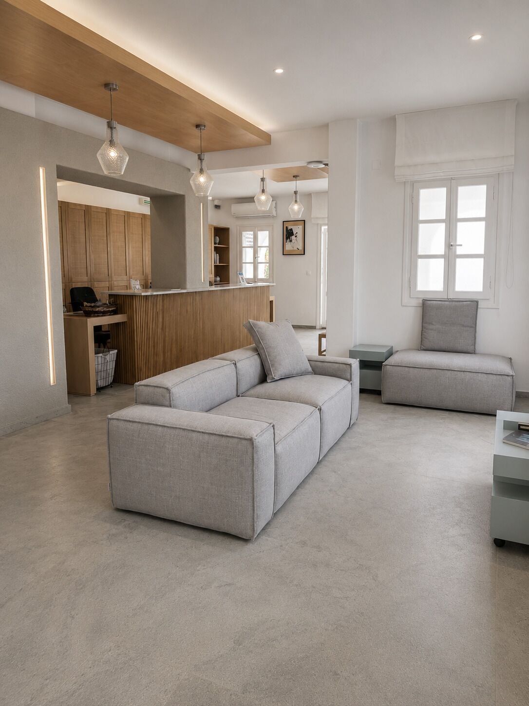 A modern living room with a sectional sofa, a small side table, and a kitchen area with wooden cabinets and a bar counter.