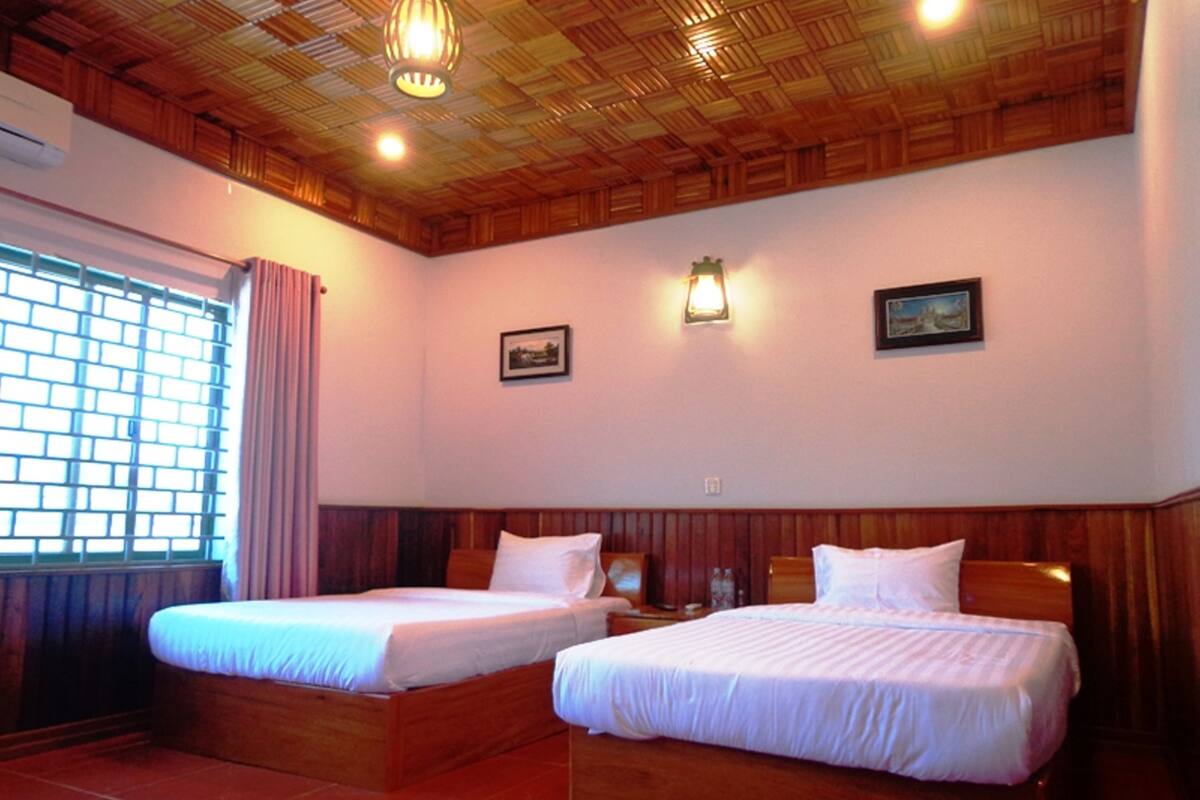 A room with two wooden beds, a window with curtains, and a wooden ceiling.