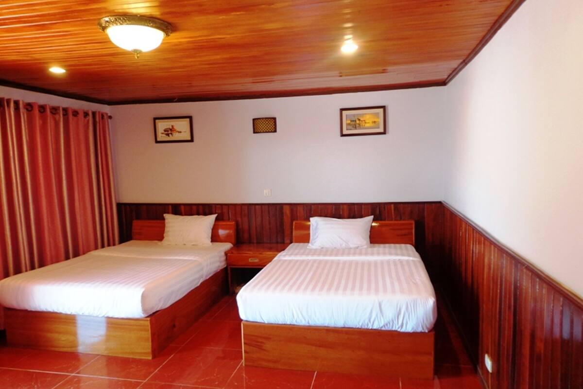 A hotel room with two beds, wooden headboards, red curtains, and a tiled floor.