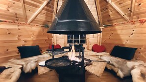 A cozy cabin interior with a central wood-burning stove, wooden walls, and fur-covered benches. - High Parks (Bedale)