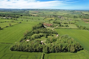 Vista aérea de un paisaje rural con campos, un pequeño pueblo y un conjunto central de árboles.