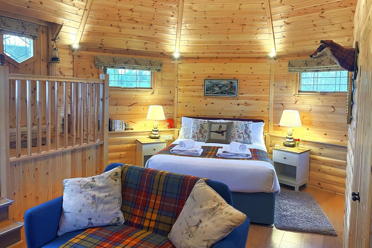 A cozy cabin-style room with a bed, a blue sofa, and a wooden ceiling.