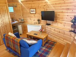 Una habitación acogedora con paredes de madera, un sofá azul, una mesita con un florero, un televisor y una ventana.