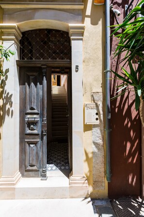 A doorway with a decorative door, a staircase leading inside, and a wall-mounted electrical box. - Anassa Estate Cultural Heritage (Rethymno)
