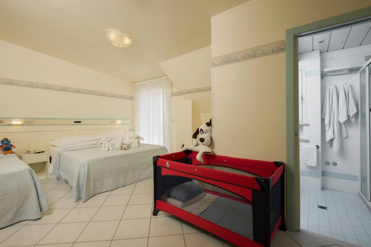 A hotel room with two beds, a red and black cabinet, and a shower area.