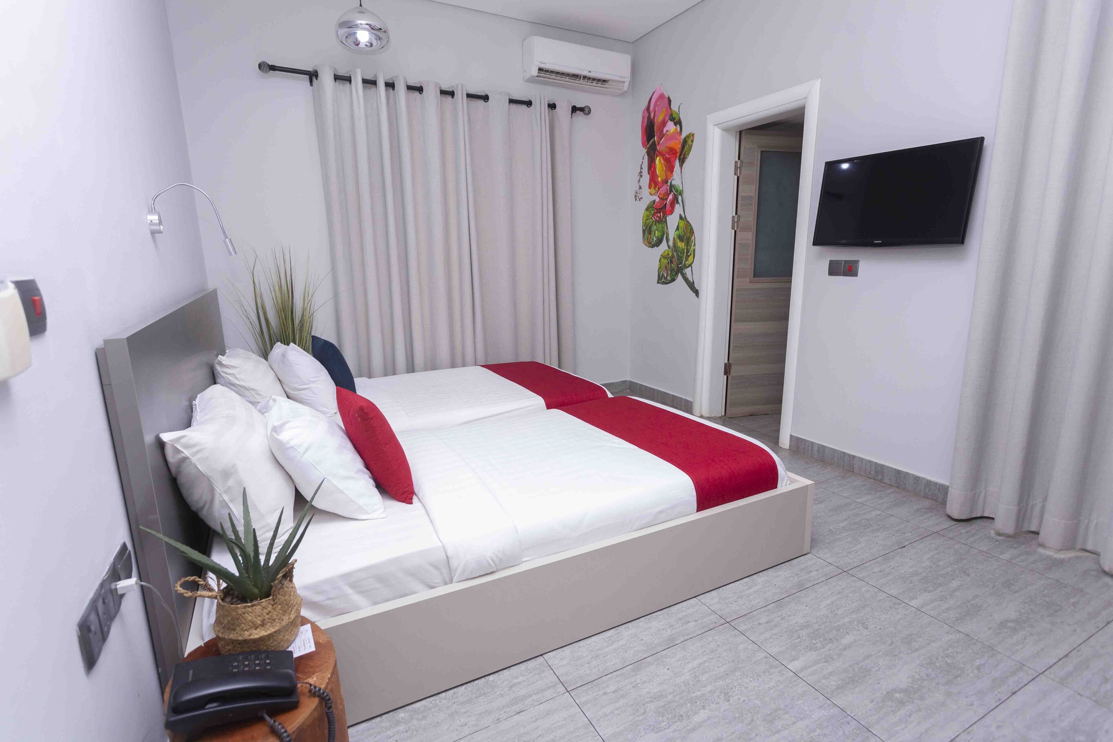 A modern hotel room with a large bed, a flat-screen TV, and a potted plant.