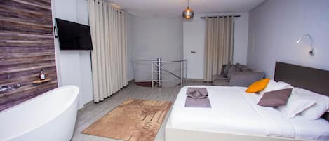 Una habitación de hotel moderna con una cama grande, un baño independiente con bañera, un televisor montado en la pared y una lámpara colgante.