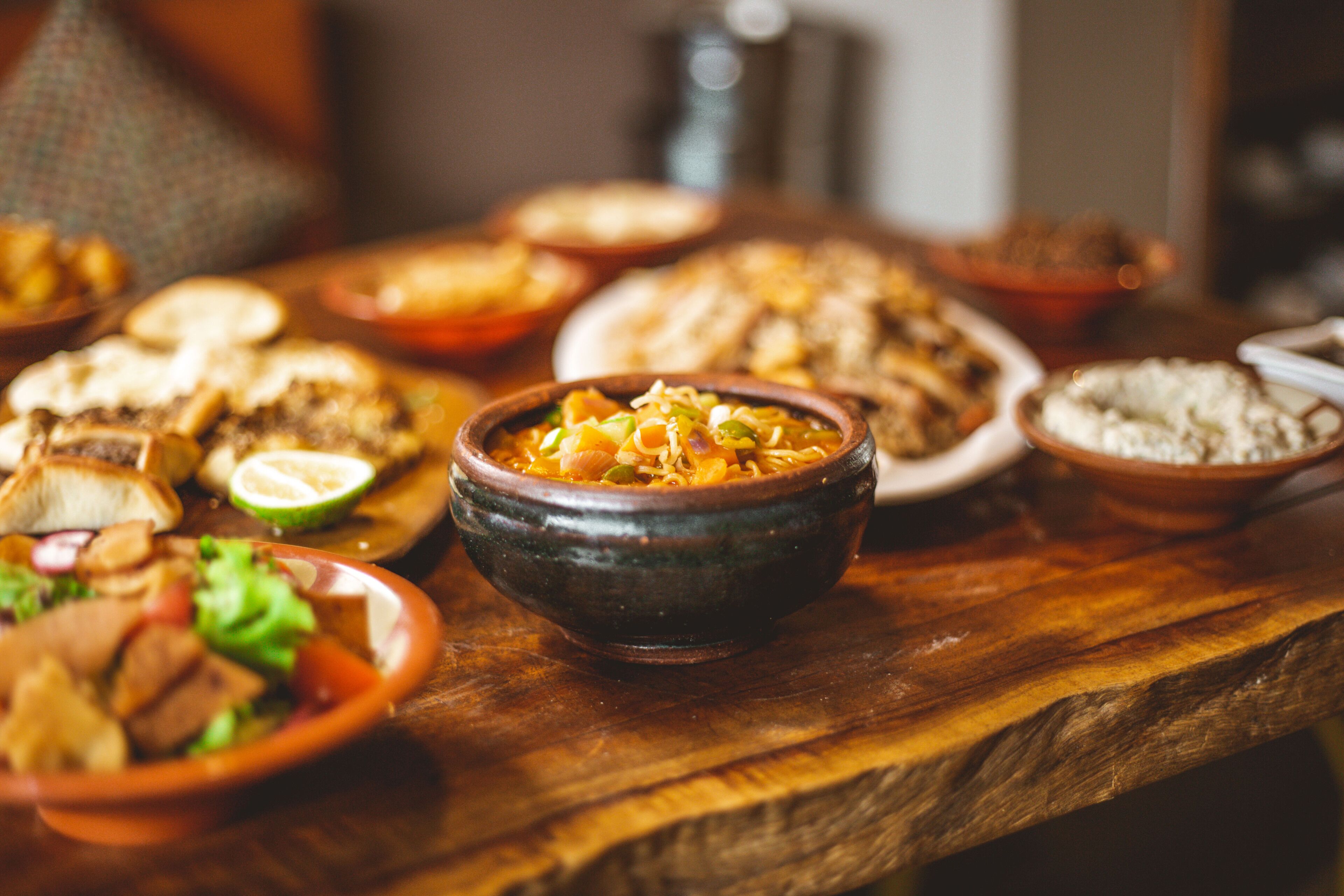 Ein Holztisch mit verschiedenen Speisen, darunter eine Schüssel Eintopf und mehrere Teller mit Essen.