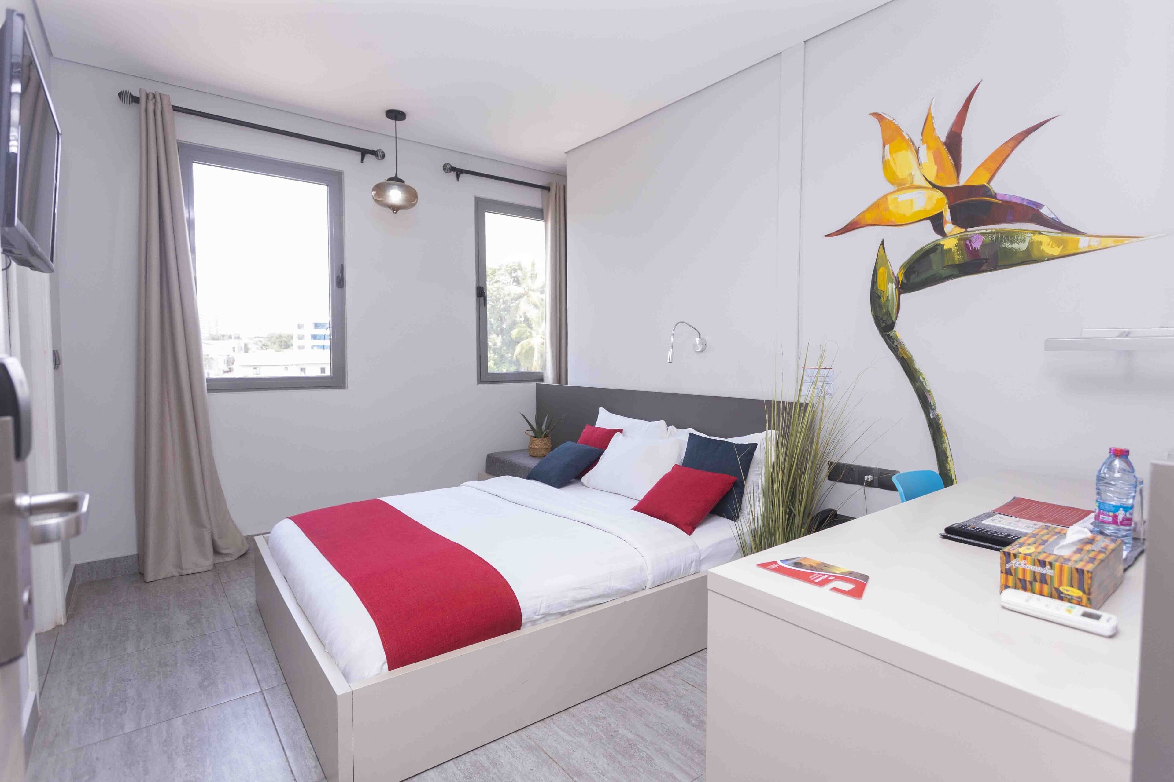 A modern hotel room with a bed, bedside table, and a desk with a chair.