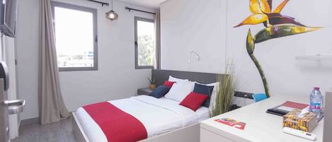 Ein modernes Hotelzimmer mit Bett, Nachttisch und Schreibtisch mit Stuhl.