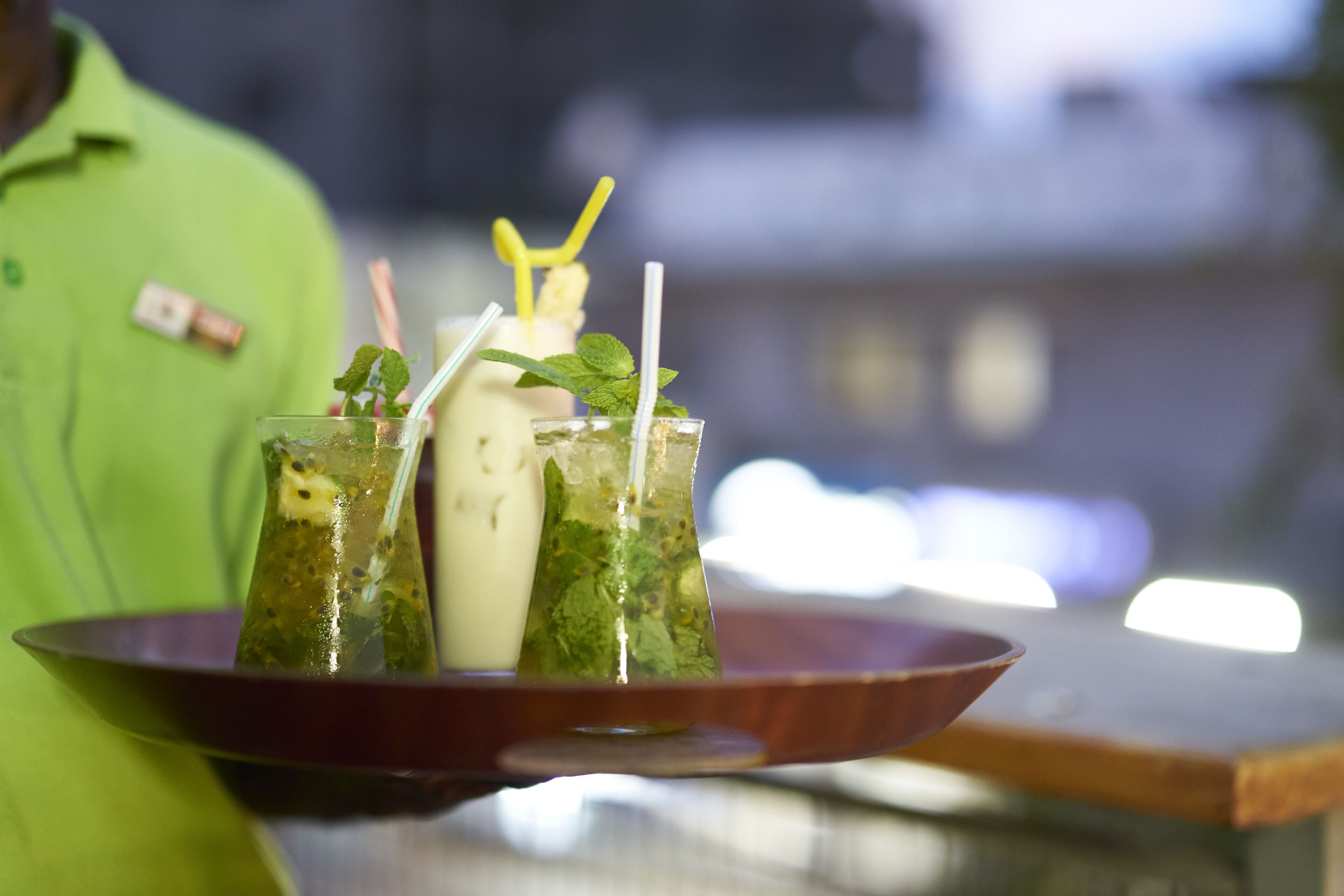A tray with three drinks, each with a straw and mint garnish, on a wooden board.