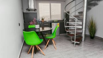 A modern kitchen with a dining area, a staircase, and a potted plant.