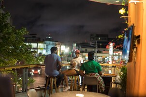 A group of people sitting at outdoor tables with a cityscape in the background.