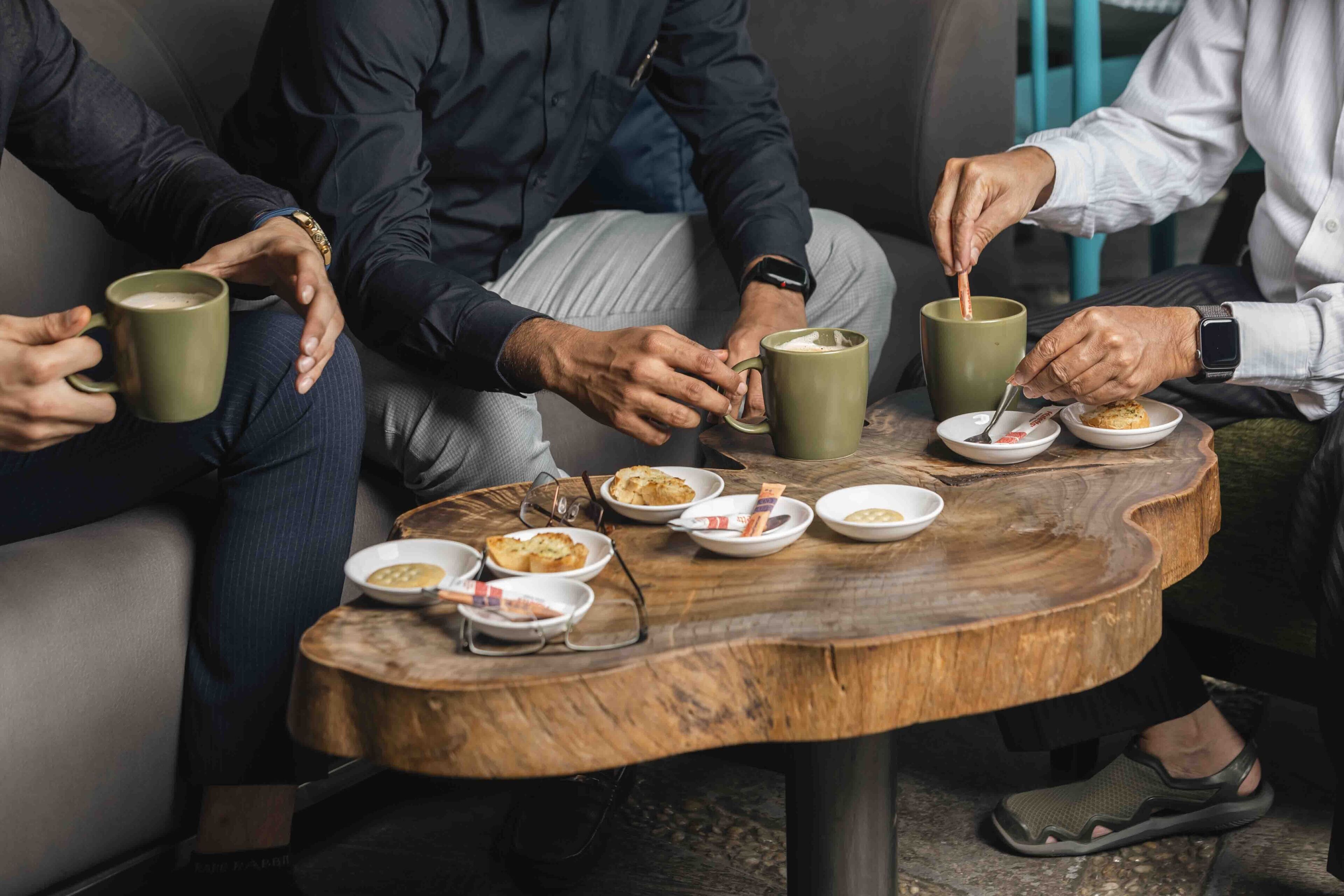 A group of people sitting around a wooden table with various dishes and mugs.