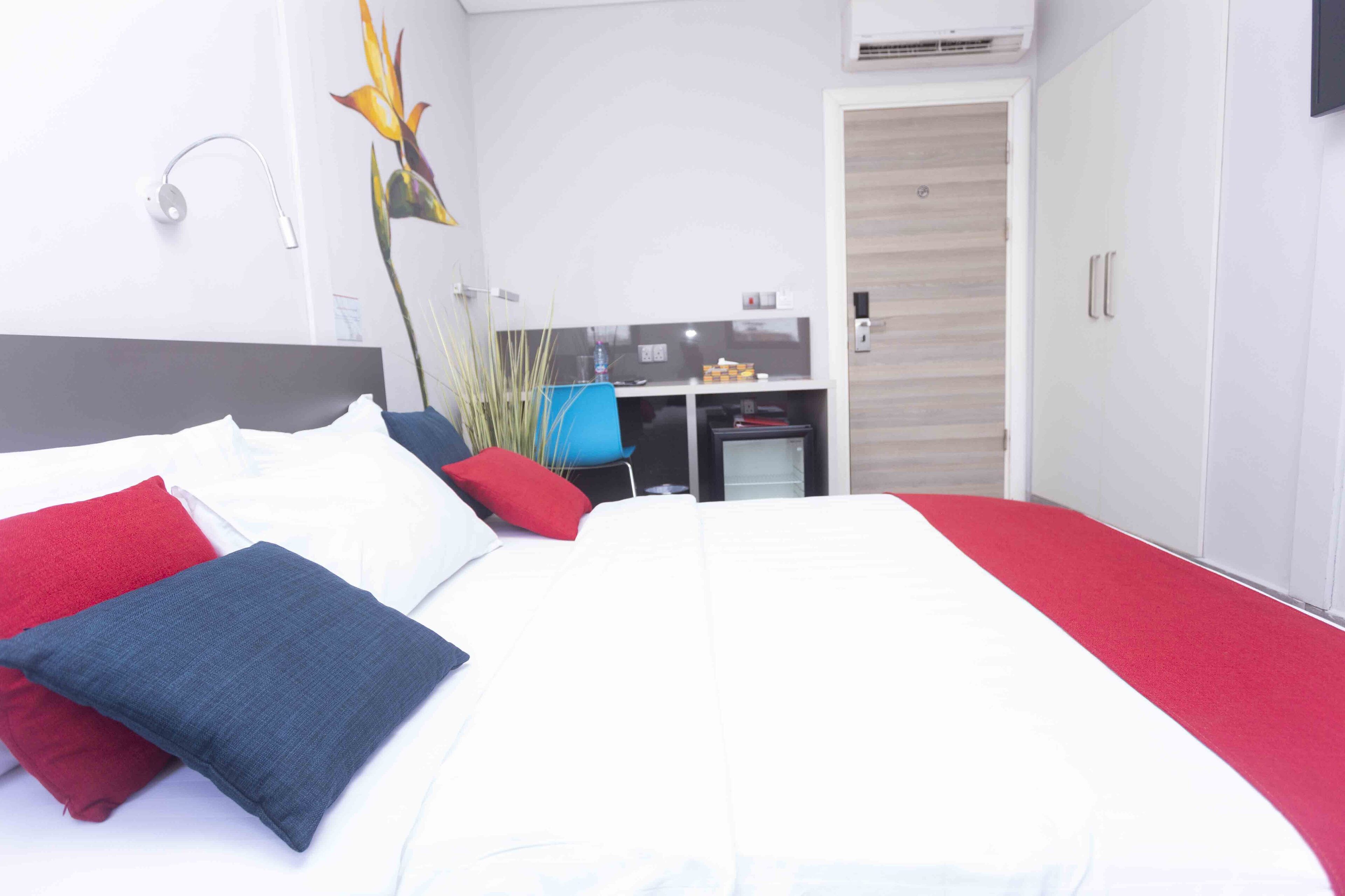 A modern hotel room with a large bed, a desk, and a wardrobe.