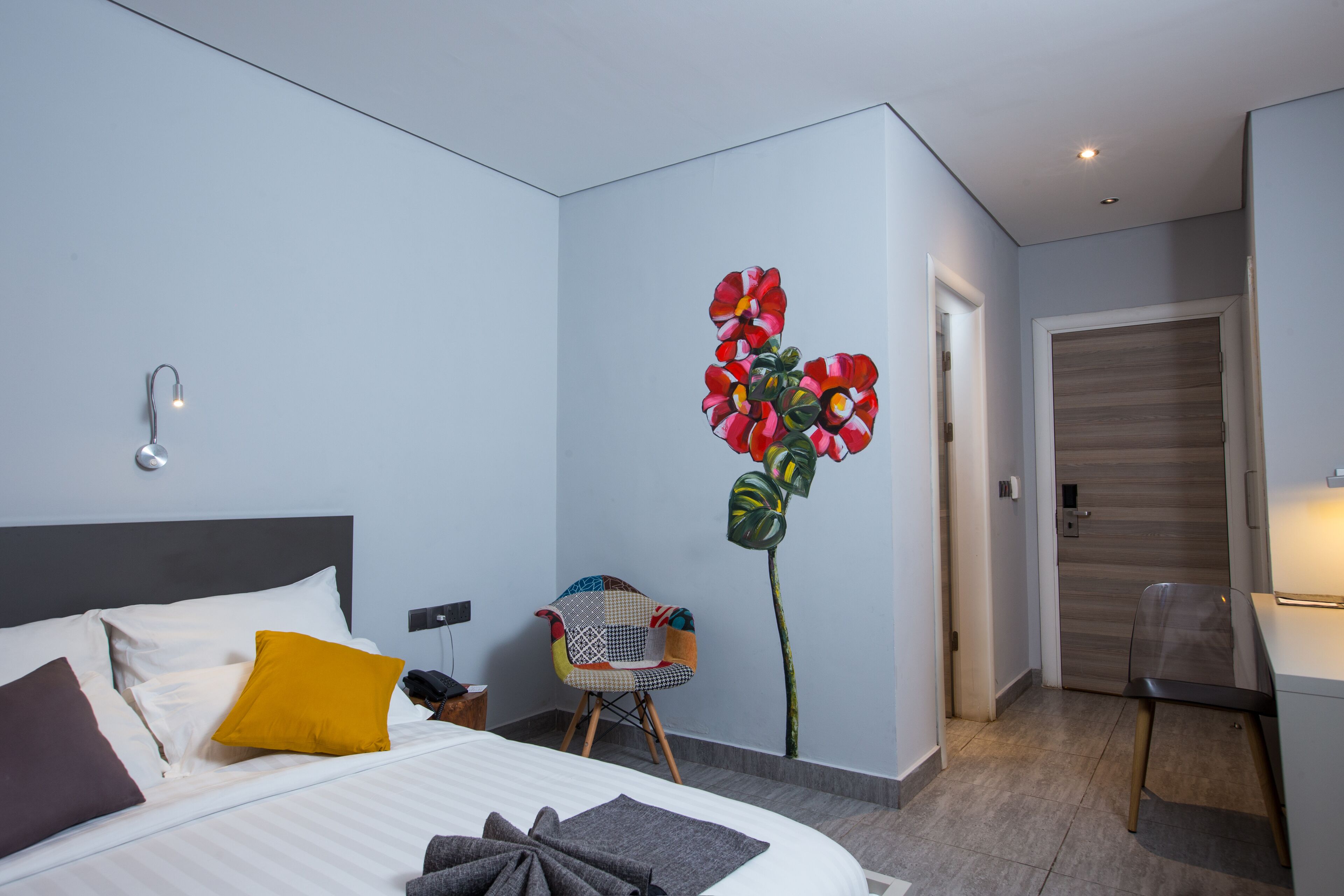 A modern hotel room with a neatly made bed, a chair, and a unique wall decoration.