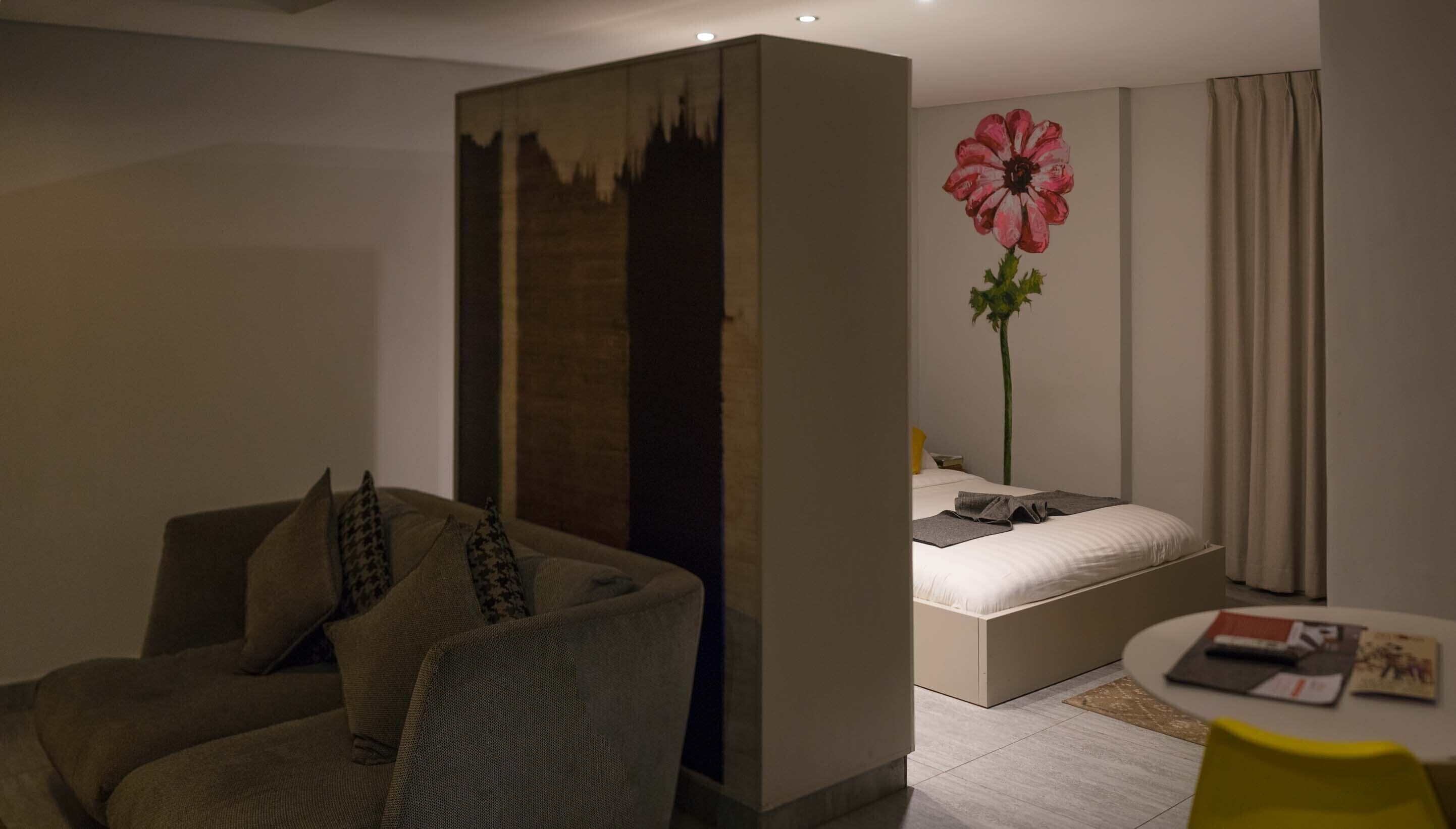A modern hotel room with a sofa, a bed, a large flower painting, and a small table.