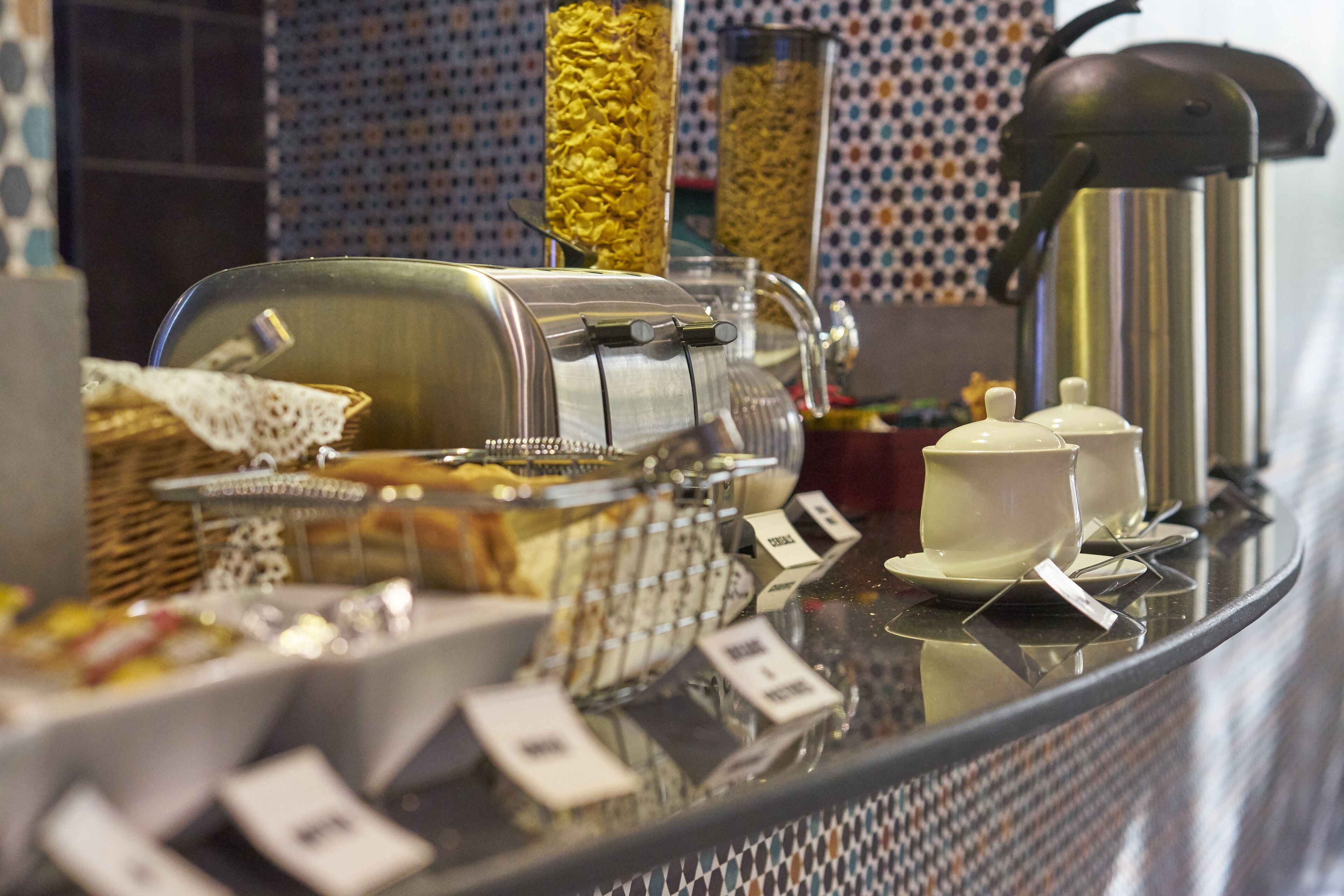 Mostrador de buffet con diferentes opciones de comida, una máquina de café y recipientes etiquetados.