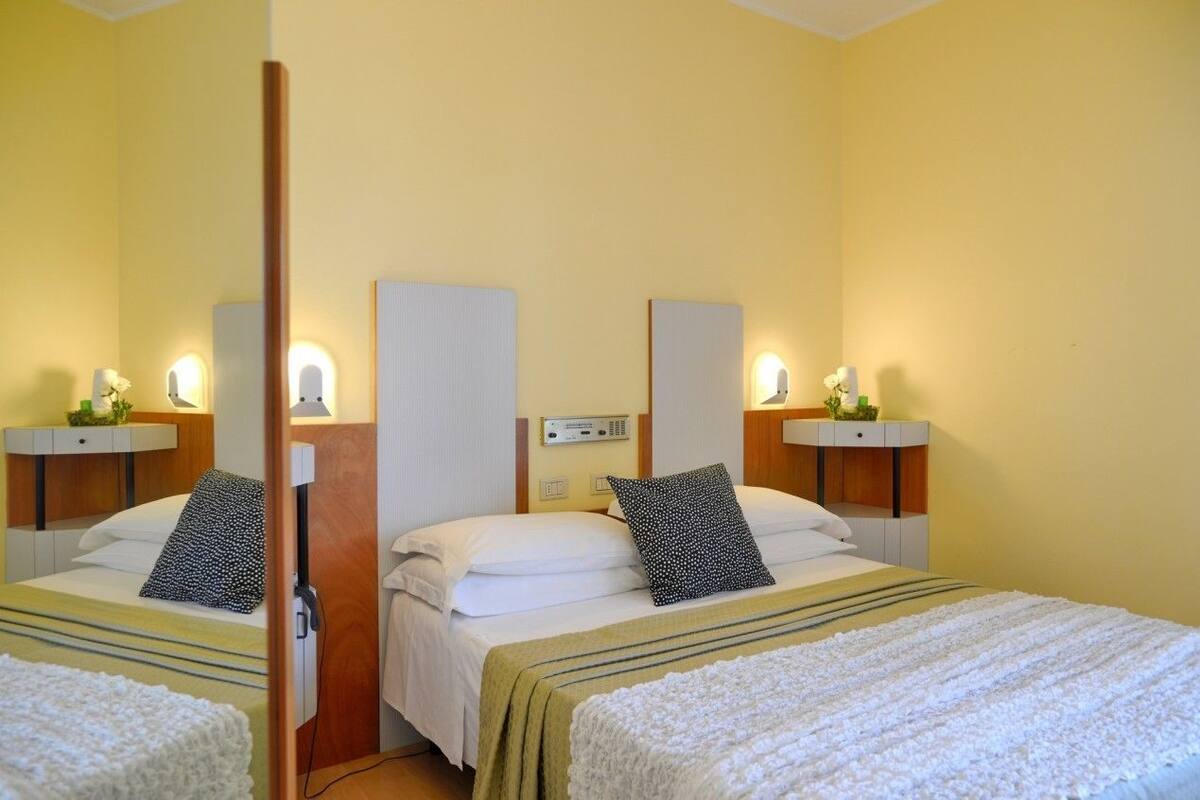 Quarto de hotel com duas camas, cada uma com mesa de cabeceira e luminária.