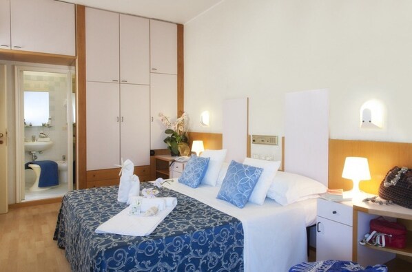 Una habitación de hotel con cama, mesita de noche, lámpara y armario.