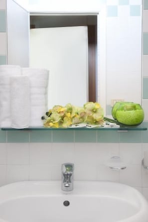 A bathroom with a white sink, a glass shelf with a green bowl and flowers, and a towel rack with white towels.